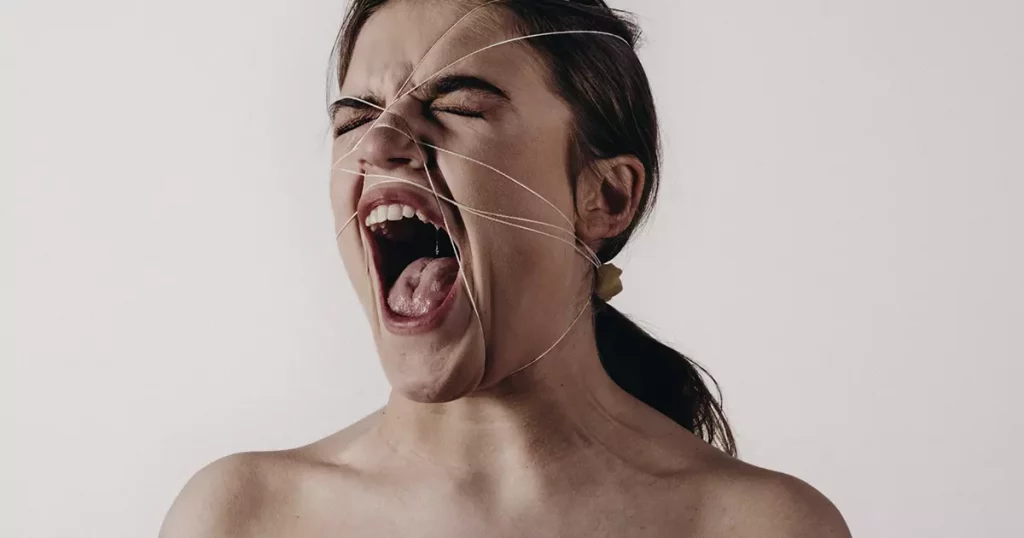 Foto de uma mulher gritando e com vários fios dando voltas em seu rosto representando os diversos tipos de violência doméstica existentes