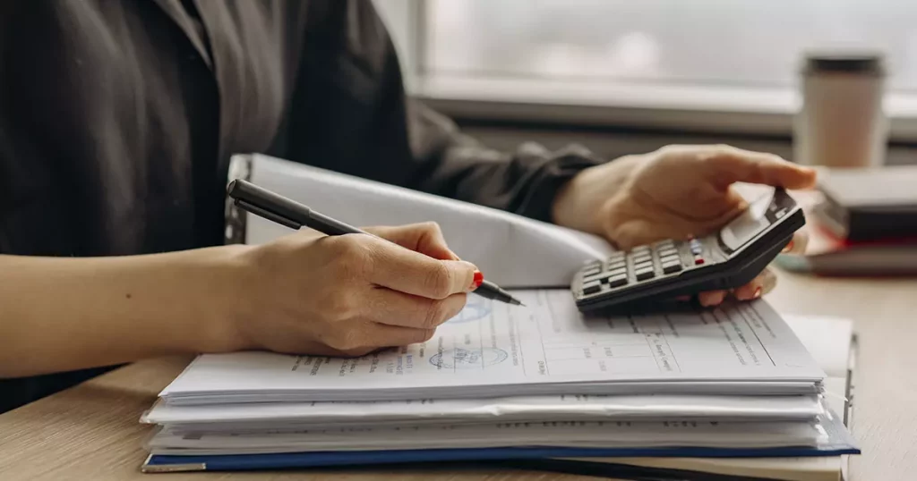 Foto de uma mulher realizando a gestão financeira do negócio de forma manual, utilizando papel e caneta, um dos erros cometidos na gestão financeira.