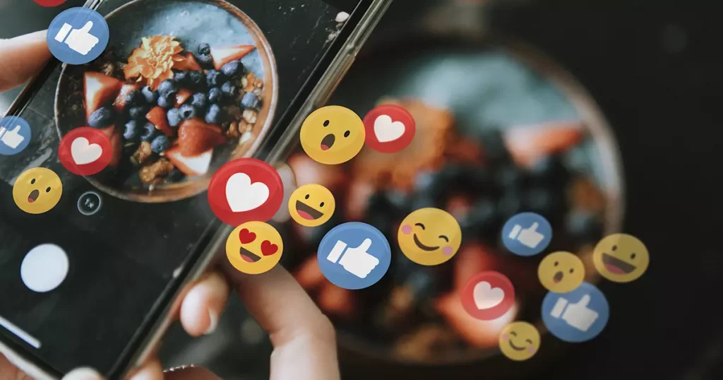 Foto de uma pessoa postando outra foto de um prato nas redes sociais com vários emojis em volta para representar a importância das redes sociais no marketing para pequenas empresas