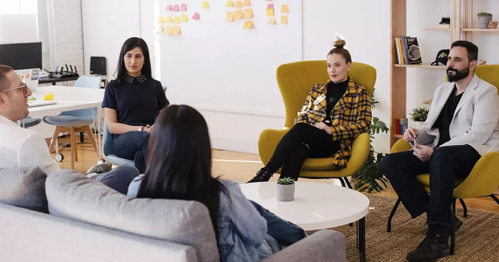 Foto de uma roda de conversa entre colaboradores de uma empresa, sendo três mulheres e dois homens, mostrando a importância de conhecer o perfil dos funcionários para uma boa gestão de benefícios.