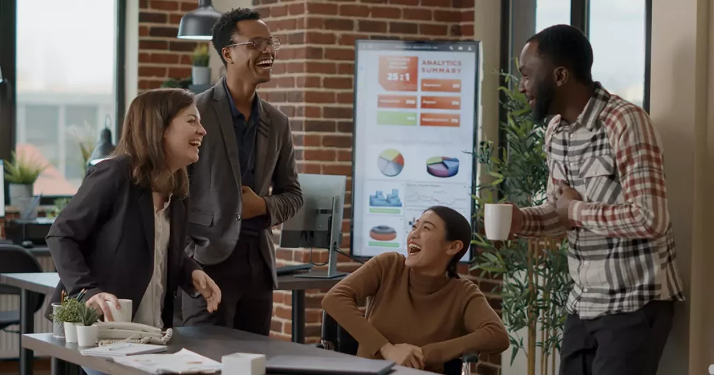 Foto de um time de funcionários felizes composto por dois homens negros, uma mulher oriental e uma mulher branca, mostrando como é importante promover a diversidade nas empresas.