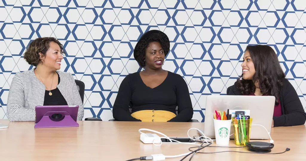Foto de três mulheres sentadas a uma mesa, com um tablet e um notebook as suas frentes, se atualizando e estudando oportunidades de negócio para serem empreendedoras de sucesso.