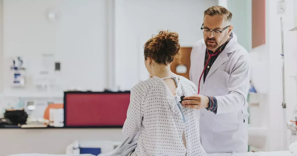 Foto de um médico auscultando a parte de trás do tronco de uma paciente em um consultório mostrando a qualidade no atendimento do plano de saúde Bradesco empresarial