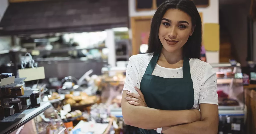 Foto de uma mulher morena, de cabelos longos, blusa branca e avental verde escuro, representando a importância de conhecer o perfil dos funcionários para escolher o plano de saúde ideal.