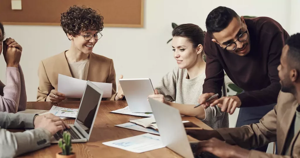 Foto de seis pessoas em volta de uma mesa de reunião, todos felizes, mostrando como uma boa gestão de benefícios corporativos pode motivar os funcionários de uma empresa
