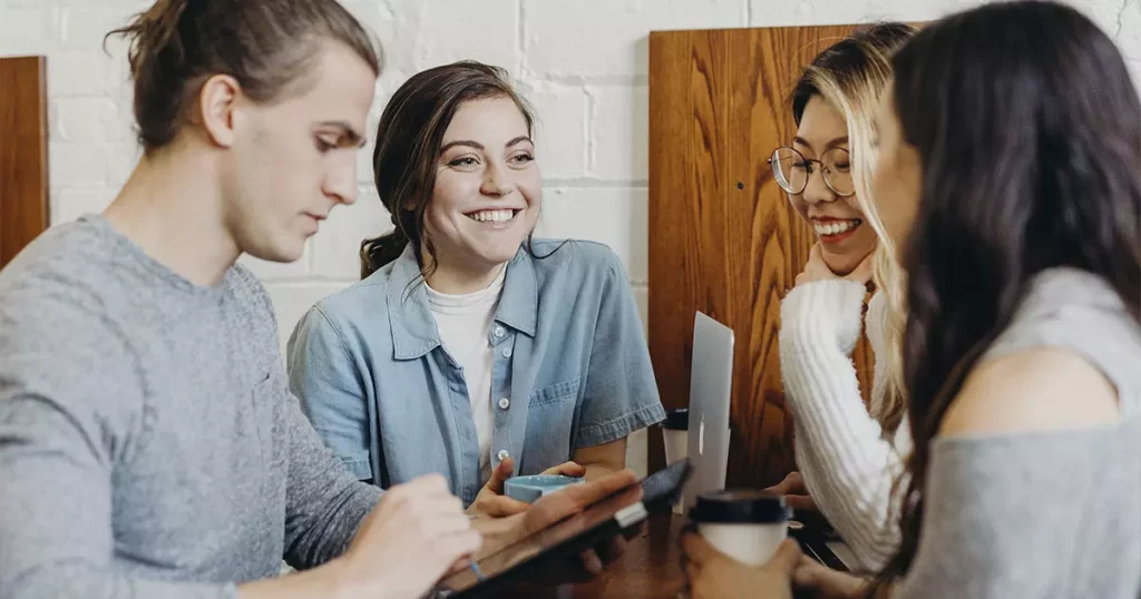 Foto de três mulheres e um homem, felizes em volta de uma mesa de trabalho, representando a satisfação dos funcionários que têm seguro de vida empresarial