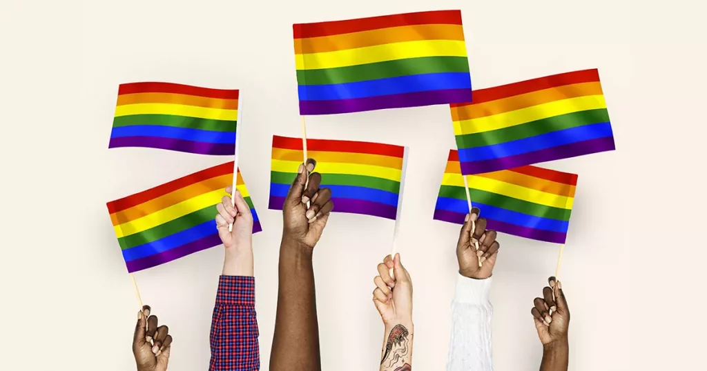 Seis mãos diversas levantando bandeiras do arco-íris representando diversidade e inclusão