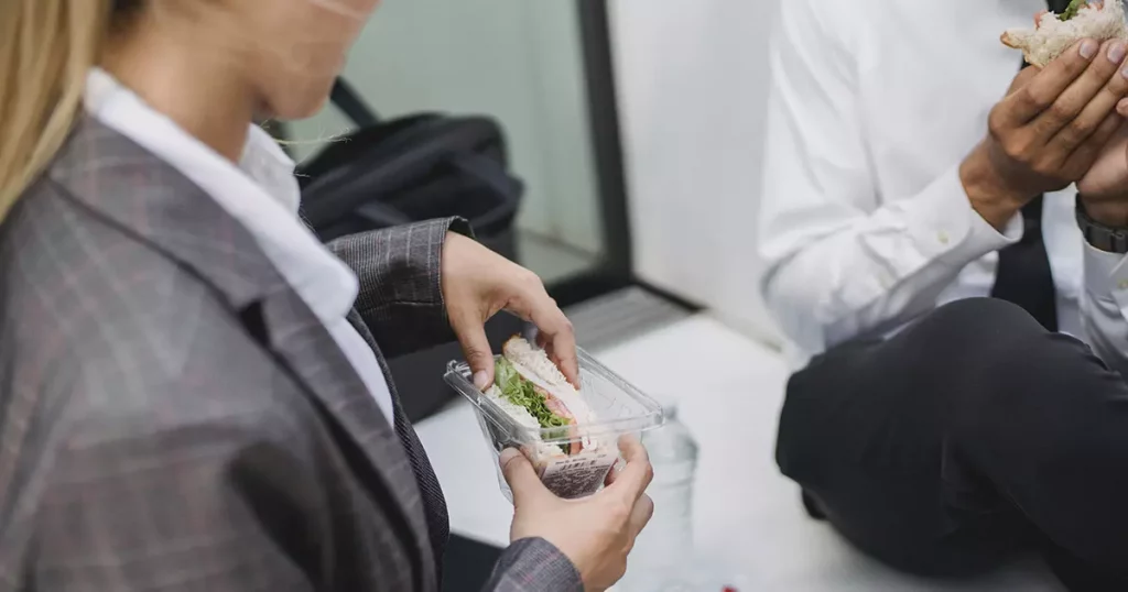 Duas pessoas lanchando sanduíche natural no trabalho representando a dica de incentivar uma boa alimentação para promover o bem-estar no trabalho