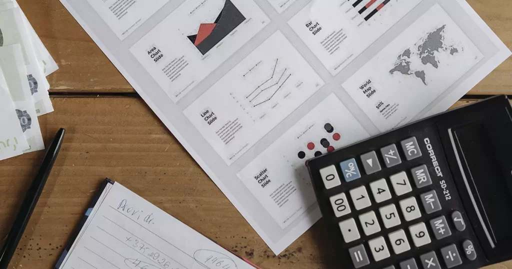 Foto de um papel com gráficos e planilhas, um calculadora preta e um outro papel com anotações representando o controle de fluxo de caixa para gestão financeira para pequenas empresas
