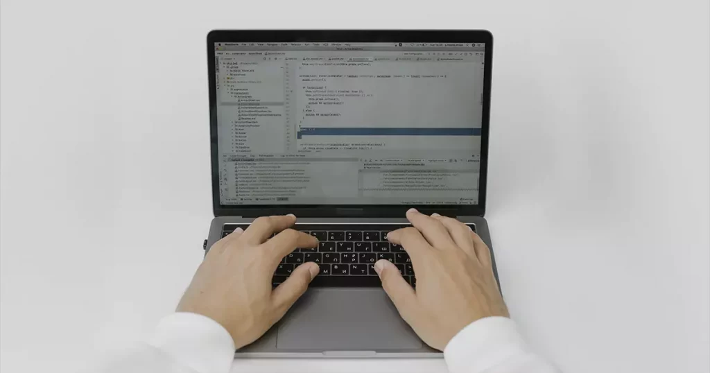 Foto de um notebook aberto com códigos em sua tela e duas mãos sobre seu teclado representando a importância do seguro cibernético para os sistemas de segurança das empresas
